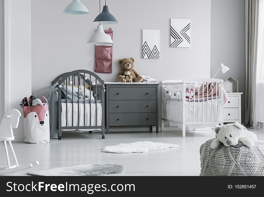 Brown Teddy Bear On Grey Wooden Commode Between Two Cribs In Fashionable Bedroom For Twins