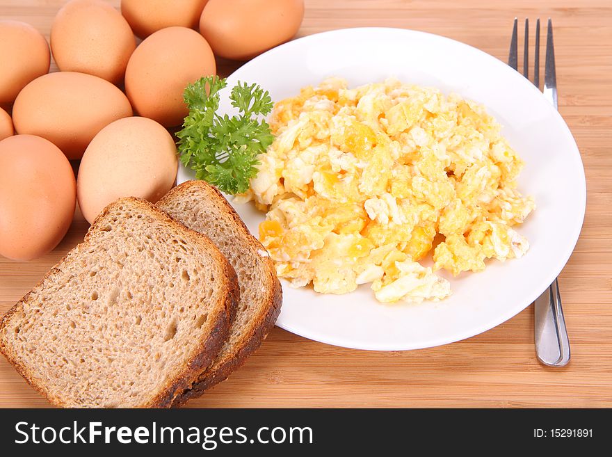 Scrambled eggs, some fresh eggs and wholemeal bread, and a fork, decorated with parsley