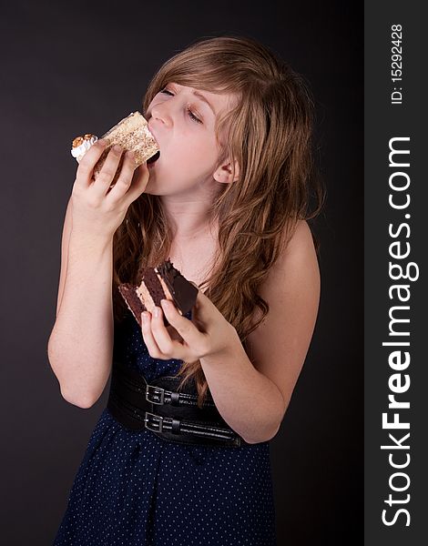 Beautiful teen girl eating cake over black background