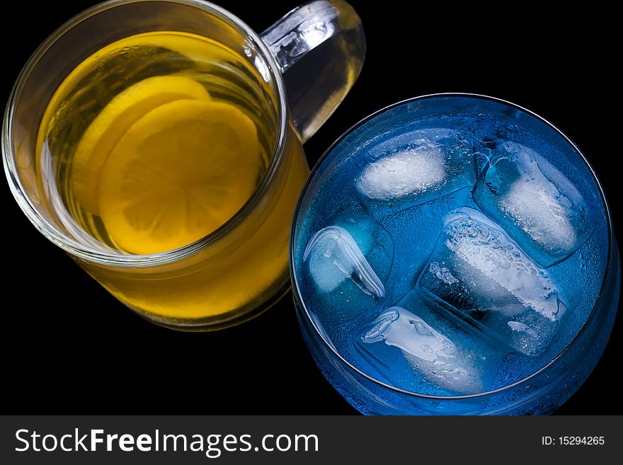 Ice tea and a blue drink with ice in a glass on a black background. Ice tea and a blue drink with ice in a glass on a black background