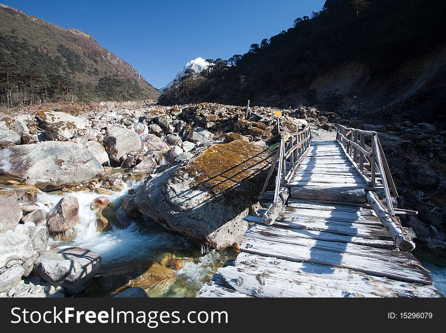 A scene of a mountain river in Sikkim, backed by snow capped peaks in the background and a lonely bridge in the foreground. A scene of a mountain river in Sikkim, backed by snow capped peaks in the background and a lonely bridge in the foreground.