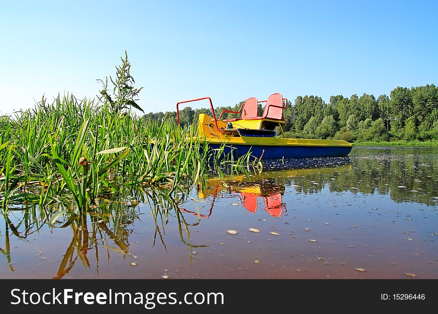 Catamaran, standing by the river in the reeds, photographed in a forest and blue sky. Catamaran, standing by the river in the reeds, photographed in a forest and blue sky