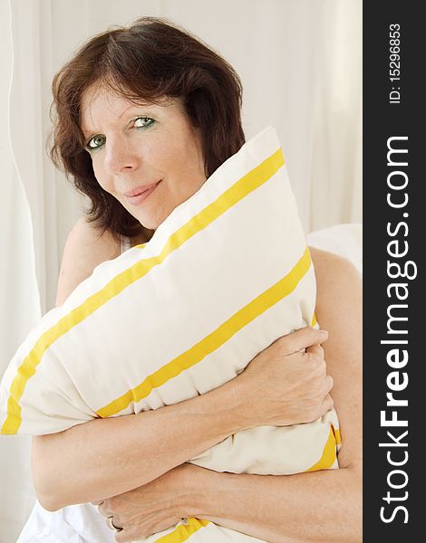 Mature woman with a pillow in her arms is looking at camera. Mature woman with a pillow in her arms is looking at camera