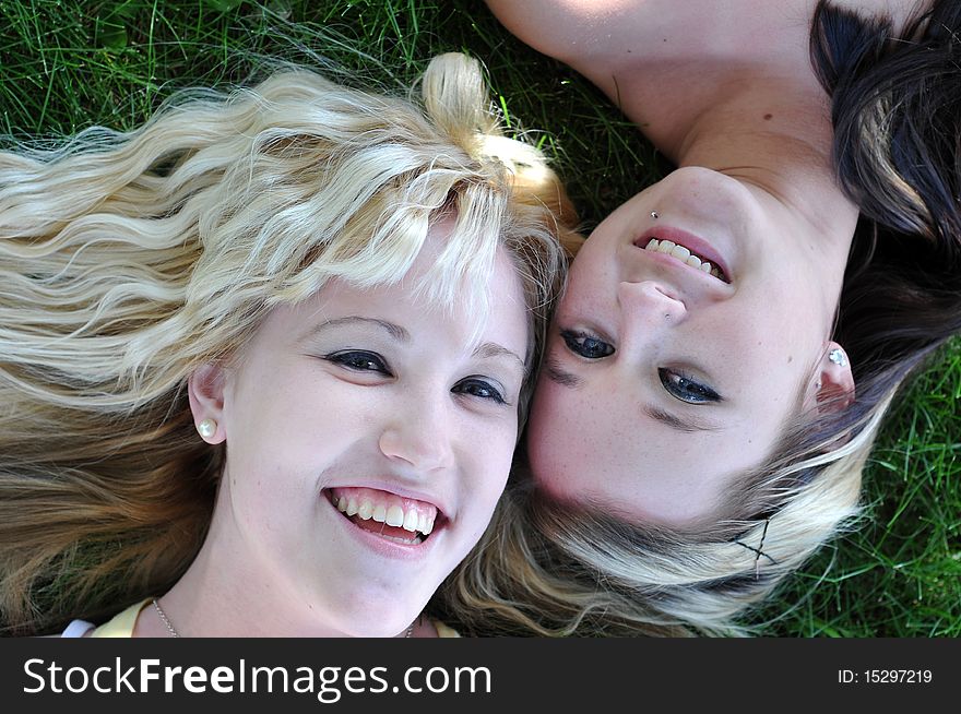 Close up of two lovely young teenage girls laying in grass smiling and laughing together. Close up of two lovely young teenage girls laying in grass smiling and laughing together.