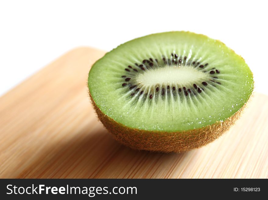 Half slice of a kiwi on wooden cutting board.