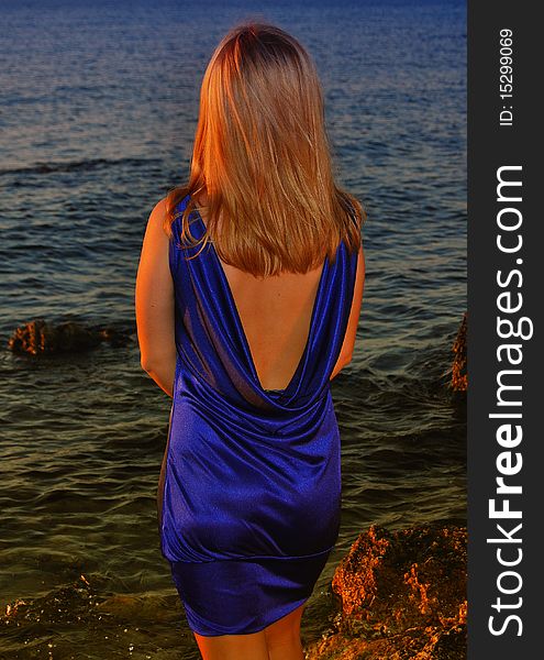 A thoughtful woman in violet dress standing on a small rock on beach. A thoughtful woman in violet dress standing on a small rock on beach