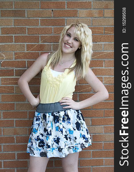 Happy young blond teenage girl standing in front of a brick wall smiling. Happy young blond teenage girl standing in front of a brick wall smiling.