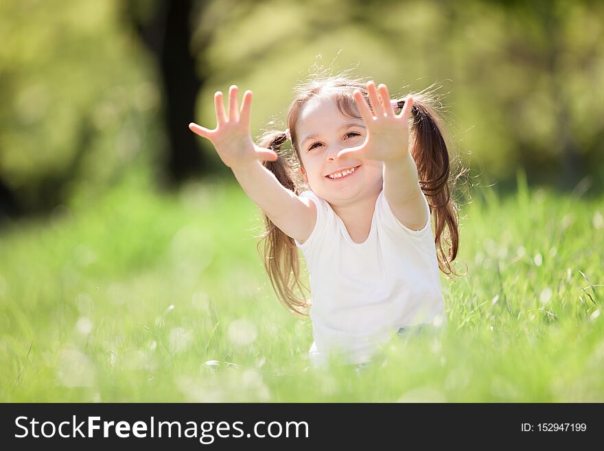 Cute little girl play in the park. Beauty nature scene with colorful background at summer or spring season. Family outdoor lifestyle. Happy girl relax on green grass