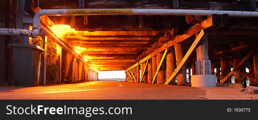 Wooden support of bridge and pier below tunnel cycleway and pedestrian crossway showing perspective in warm lighting. Wooden support of bridge and pier below tunnel cycleway and pedestrian crossway showing perspective in warm lighting