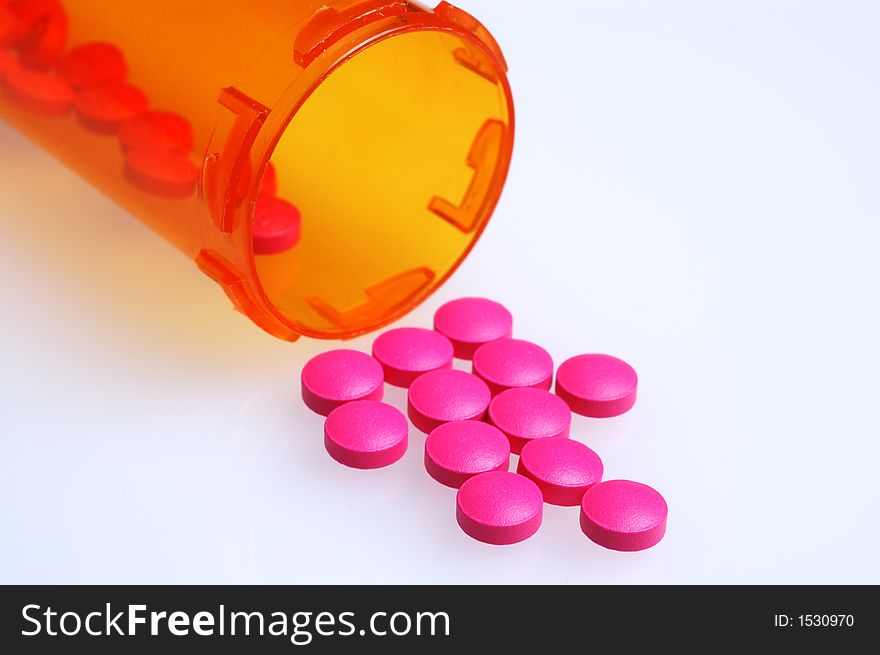 Magenta colored pills on white surface in front of the medicine bottle they spilled from. Magenta colored pills on white surface in front of the medicine bottle they spilled from