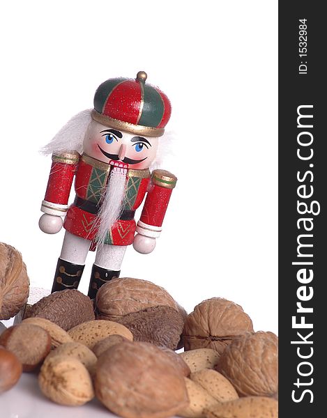A wooden nutcracker against a white background. An assortment of nuts are in the foreground.