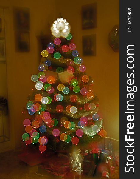 A decorated Christmas tree with gifts in a home living room. Double exposure to provide a flared abstract lighting effect. A decorated Christmas tree with gifts in a home living room. Double exposure to provide a flared abstract lighting effect.