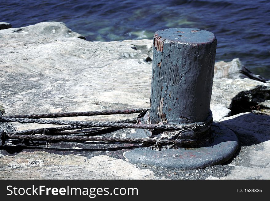 Old Broken Blue Pole With Ropes On A Rock At The Ocean