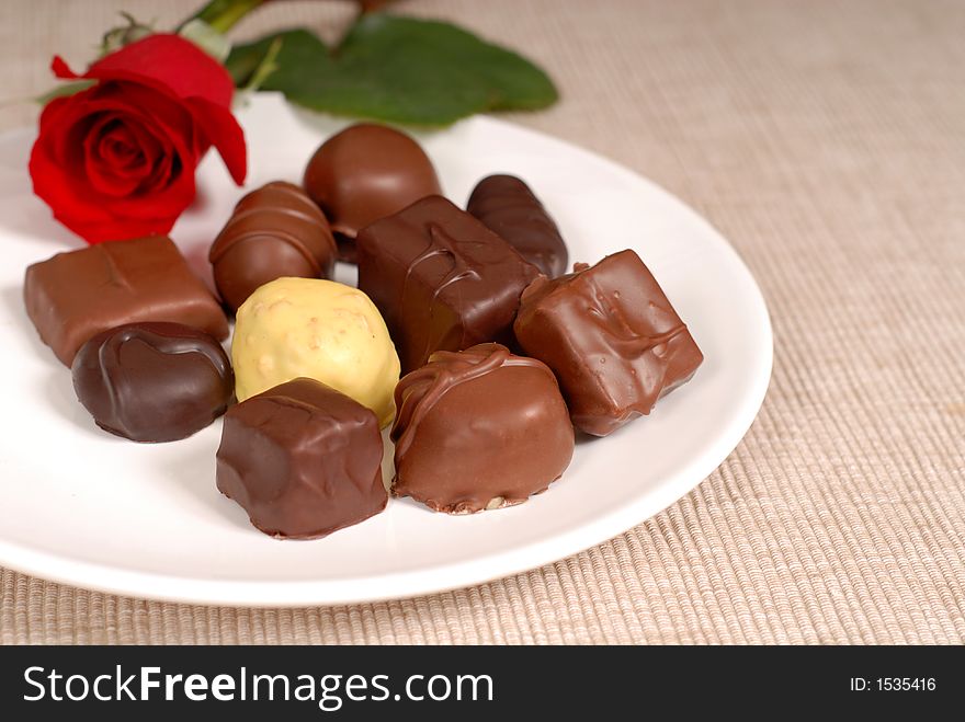 Variety of chocolates and a rose on a white plate