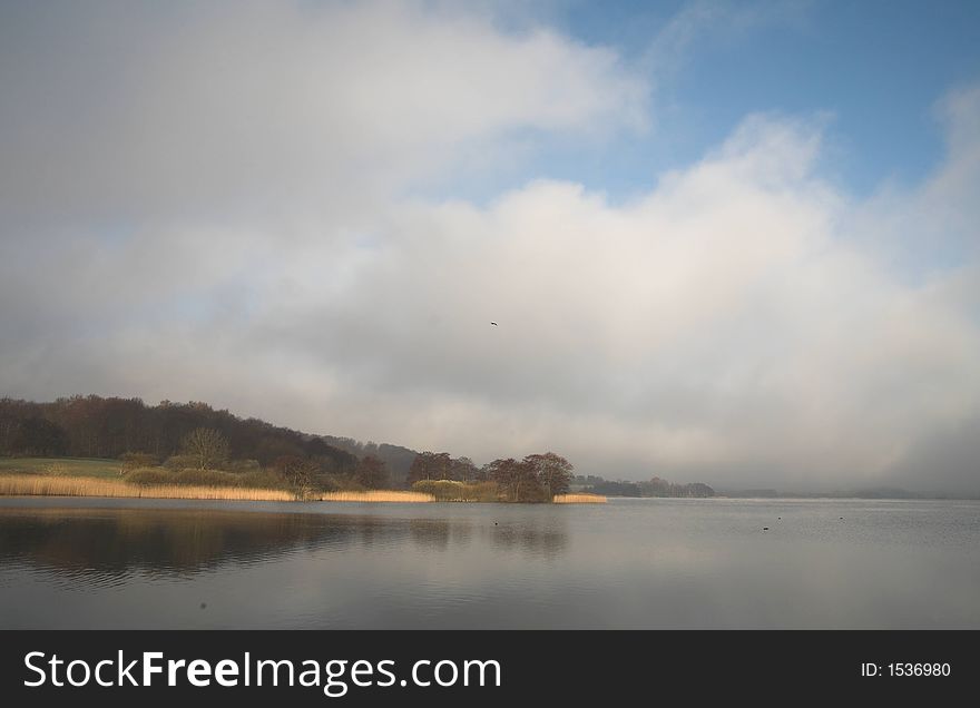 A lake in denmark in the winter time with a foggy weather