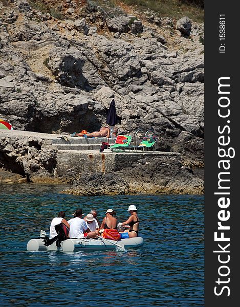 Plastic boat with motor take a group of swimmers on the rock