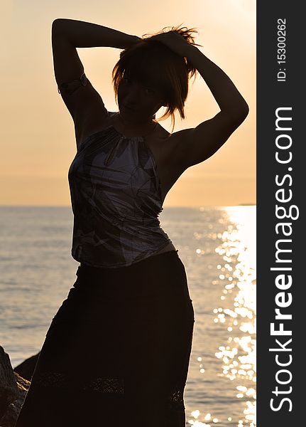 Silhouette of a young woman with slim figure doing his hair against sea; warm lighting setup. Silhouette of a young woman with slim figure doing his hair against sea; warm lighting setup
