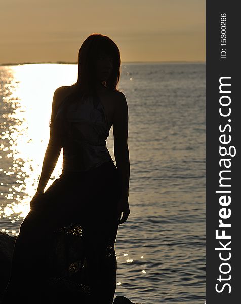 Silhouette of a young woman with slim figure against sea; warm lighting. Silhouette of a young woman with slim figure against sea; warm lighting