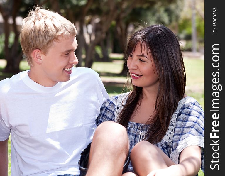 Young romantic couple sitting together and having fun in the park over natural background