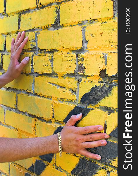 Hands of the young man are touching the wall. There is a yellow bracelet on right arm. Hands of the young man are touching the wall. There is a yellow bracelet on right arm.