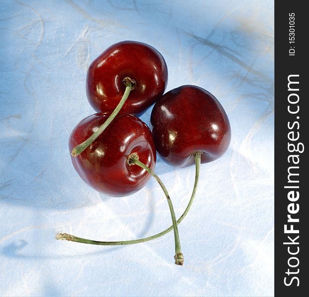 Closeup of three cherries on textured surface with blue shadows