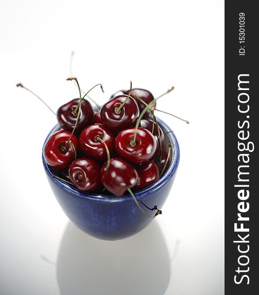 Closeup of fresh cherries in blue ceramic bowl on white reflective surface using selective focus. Closeup of fresh cherries in blue ceramic bowl on white reflective surface using selective focus