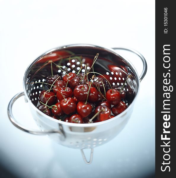 Fresh cherries in colander on white reflective surface using selective focus