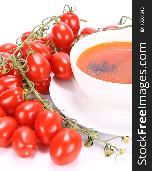 Tomato soup decorated with pepper with fresh tomatoes around it and a spoon