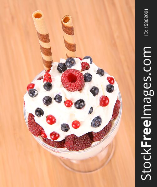 Whipped cream with raspberries, red currants and blue berries in a glass cup, decorated with a wafer tube on wooden background. Whipped cream with raspberries, red currants and blue berries in a glass cup, decorated with a wafer tube on wooden background