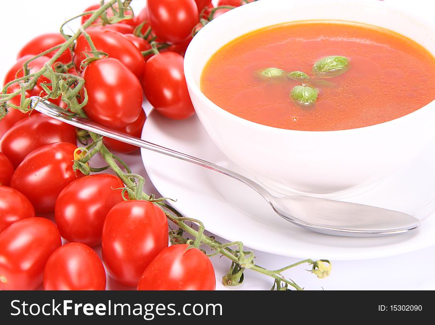 Tomato soup decorated with basil leaves with fresh tomatoes around it and a spoon