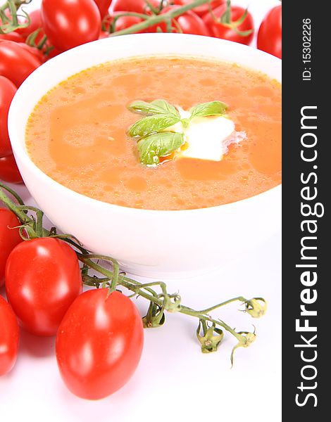 Tomato soup decorated with basil and cream with fresh tomatoes around it