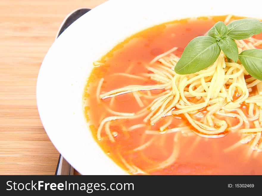 Tomato soup decorated with basil leaves with a spoon on wooden background