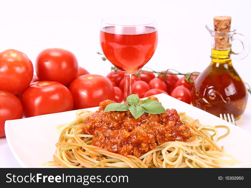 Colorful spaghetti bolognese on a plate, some fresh tomatoes, olive oil and a glass of pink wine