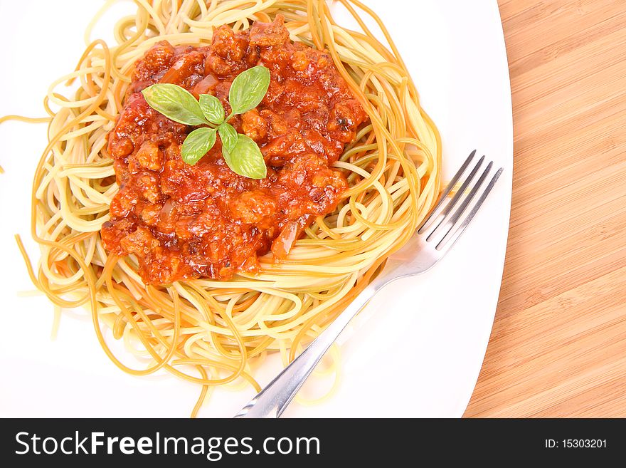 Colorful spaghetti bolognese on a plate decorated with basil leaves and a fork on a wooden background