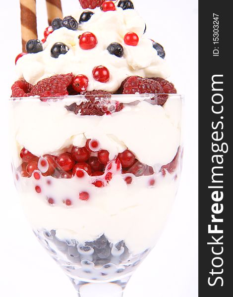 Whipped cream with raspberries, red currants and blue berries in a glass cup, decorated with a wafer tube in close up. Whipped cream with raspberries, red currants and blue berries in a glass cup, decorated with a wafer tube in close up