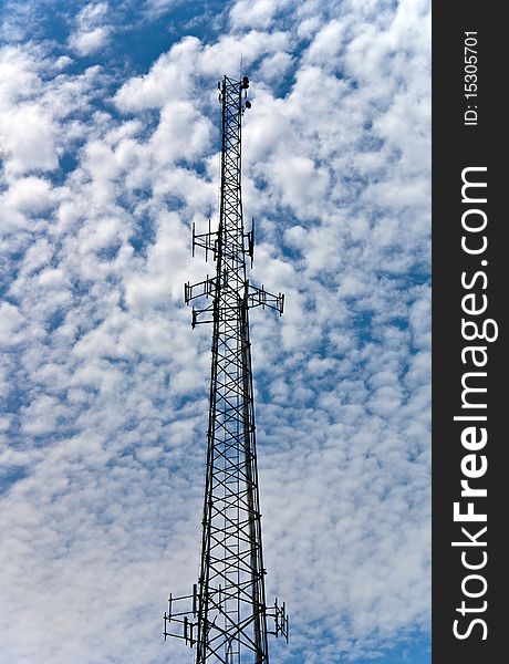 A communication tower against at fluffy cloud filled blue sky.
