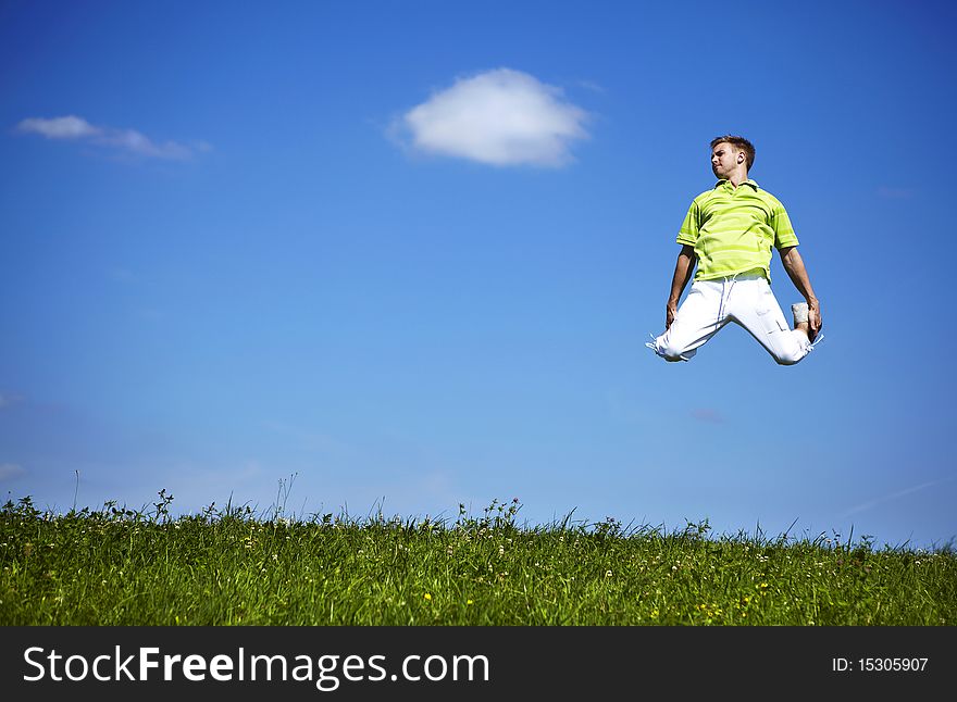 Jumping Up Guy In A Green Shirt Against Blue Sky.