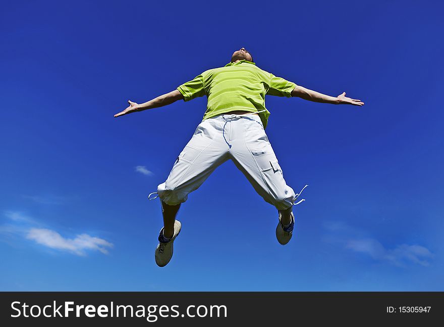 Jumping Up Guy In A Green Shirt Against Blue Sky.