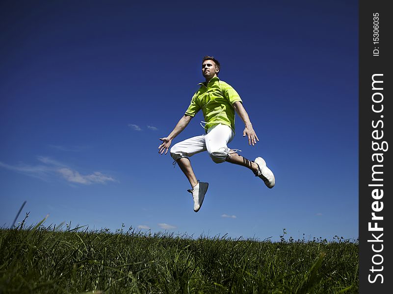 Jumping Up Guy In A Green Shirt Against Blue Sky.