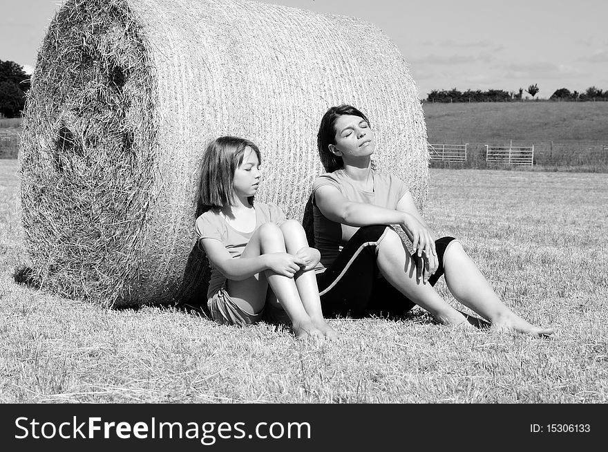 Caucasian mother and daughter relaxing near hay bales in summer season, blue sky in background. Caucasian mother and daughter relaxing near hay bales in summer season, blue sky in background