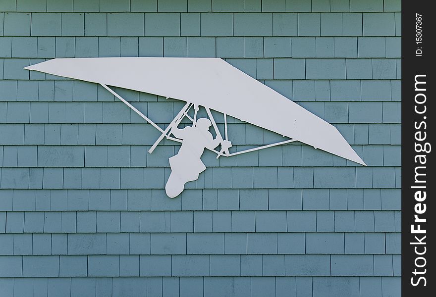 White hang gliding symbol attached to a greenish blue wooden structure. White hang gliding symbol attached to a greenish blue wooden structure