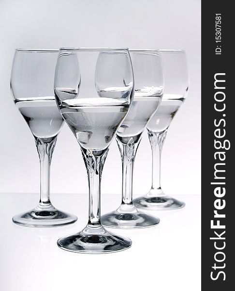 Four wine glasses half full of a clear liquid