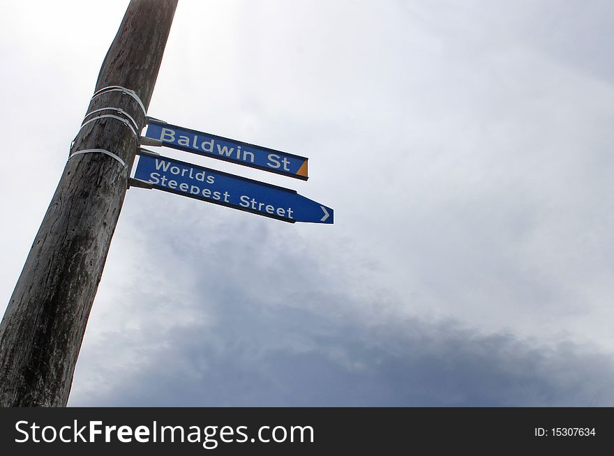 Blue street sign attached to a wooden pole. Cloudy sky in the background. Worlds Steepest Street. Metaphor for challenges faced in business, etc...