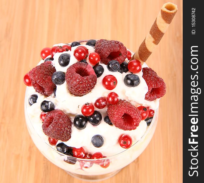 Whipped cream with raspberries, red currants and blue berries in a glass cup, decorated with a wafer tube on wooden background. Whipped cream with raspberries, red currants and blue berries in a glass cup, decorated with a wafer tube on wooden background