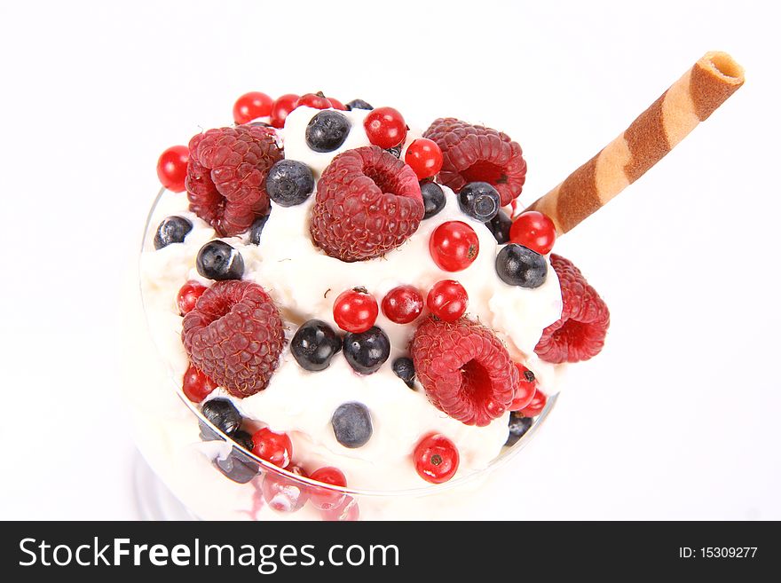 Whipped cream with raspberries, red currants and blue berries in a glass cup, decorated with a wafer tube in close up. Whipped cream with raspberries, red currants and blue berries in a glass cup, decorated with a wafer tube in close up