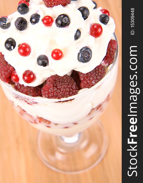 Whipped cream with raspberries, red currants and blue berries in a glass cup, on wooden background. Whipped cream with raspberries, red currants and blue berries in a glass cup, on wooden background