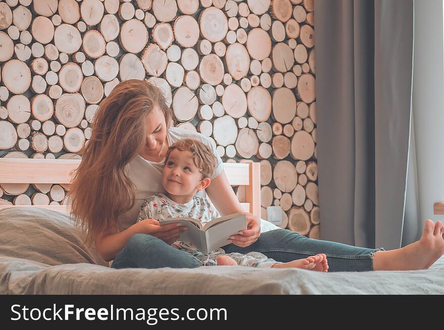 Happy loving family. Pretty young mother reading a book to her little son in modern interior