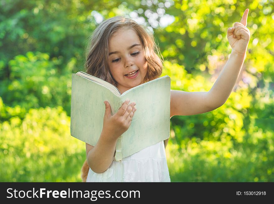 Cute industrious child is standing with a book and a briefcase outdoors. Little Girl reading the book. Place for text