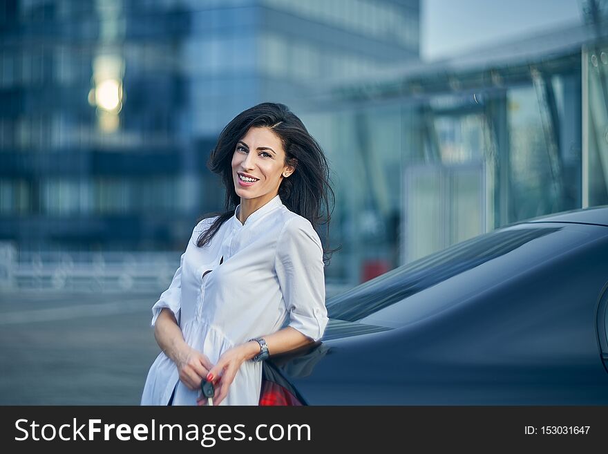 Smiling woman leaning on a car over modern office facade