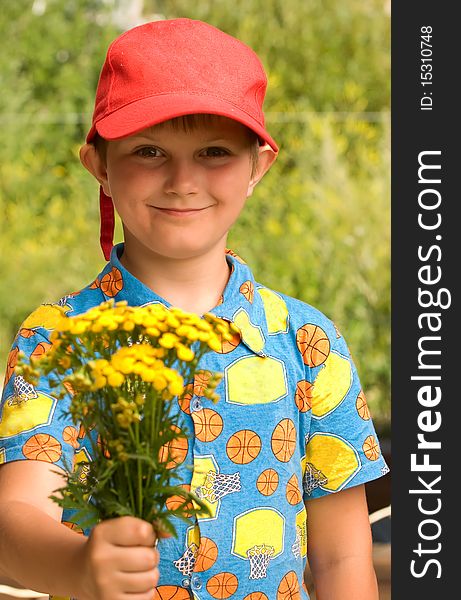 The boy stretches a bouquet of wild flowers, camomiles. The boy stretches a bouquet of wild flowers, camomiles